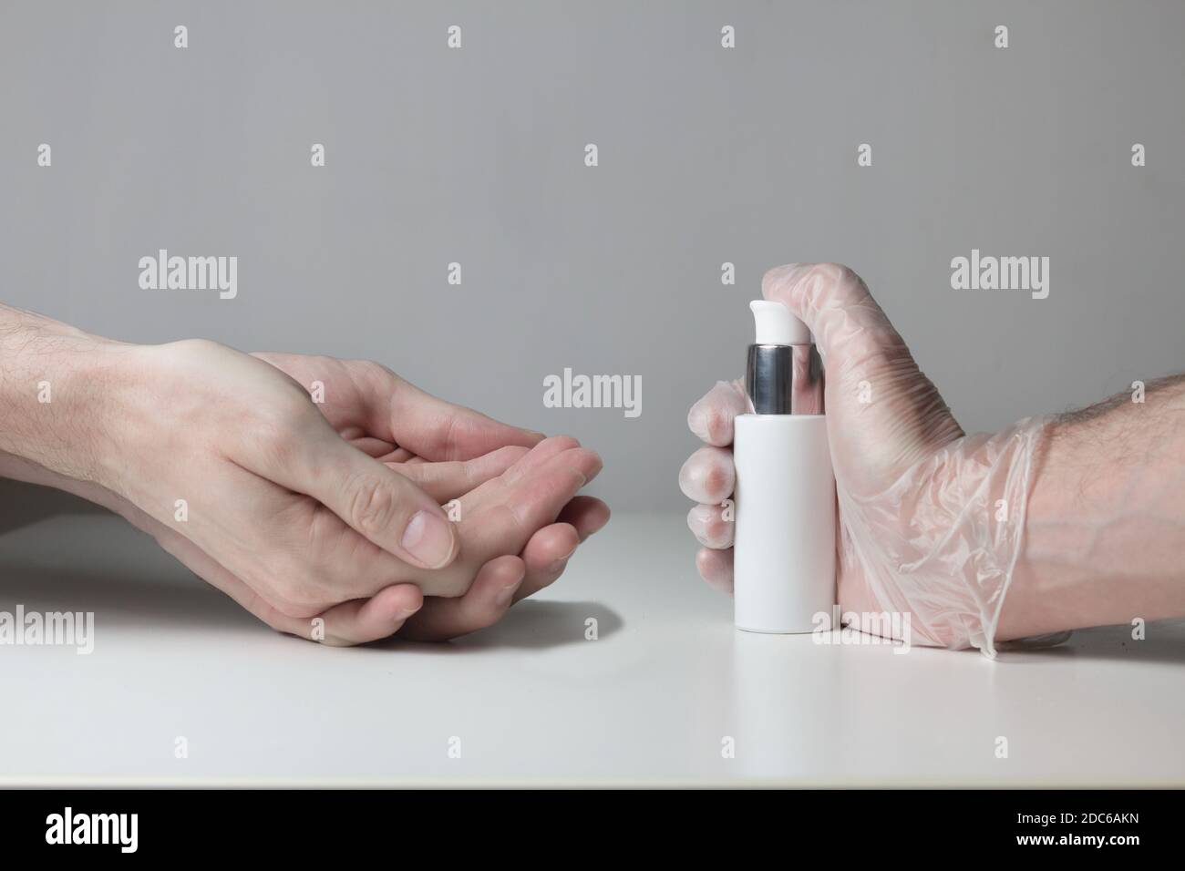 Un paio di mani aspettano di essere disinfettate da un gel idroalcolico pressato da una mano protetta da guanti semitrasparenti su fondo bianco. Foto Stock