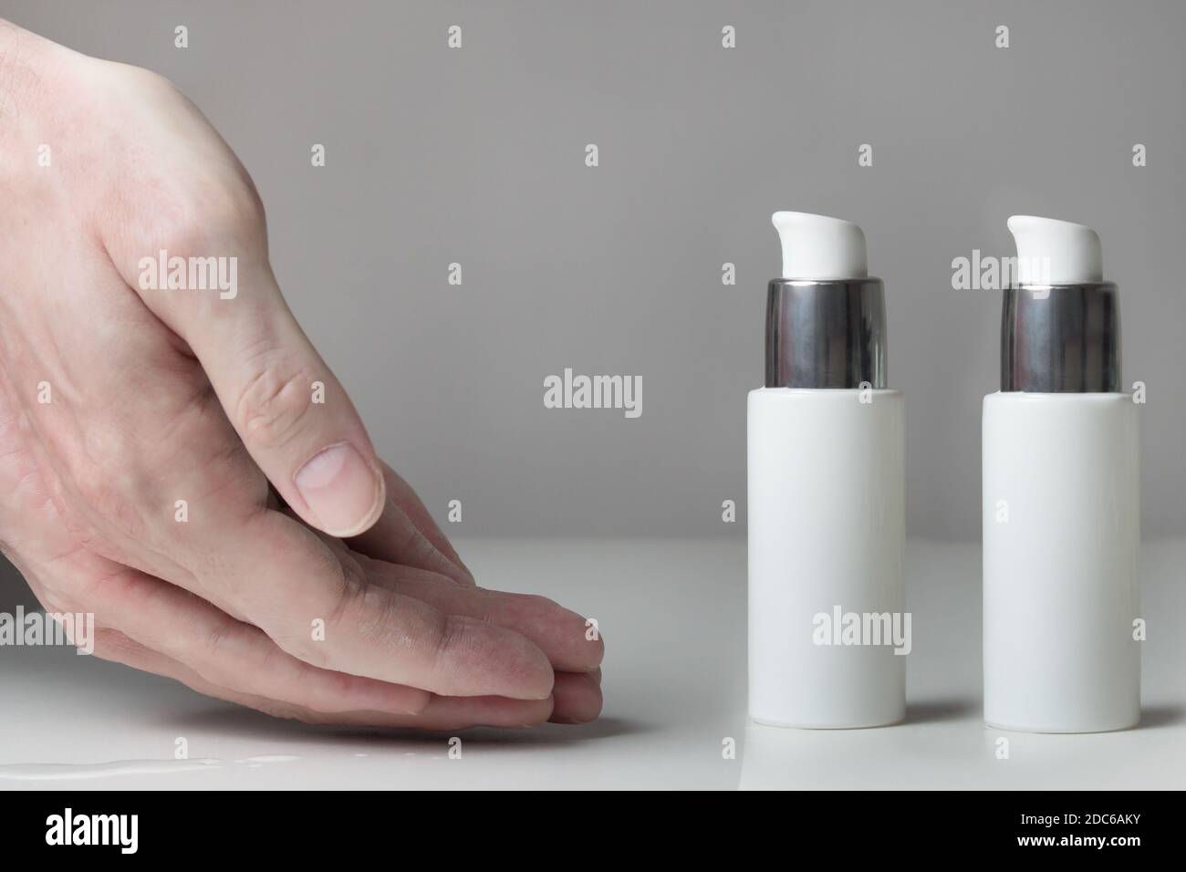 Primo piano di un paio di mani sporche allungate davanti a 2 bottiglie di gel igienizzante idroalcolico. Foto Stock