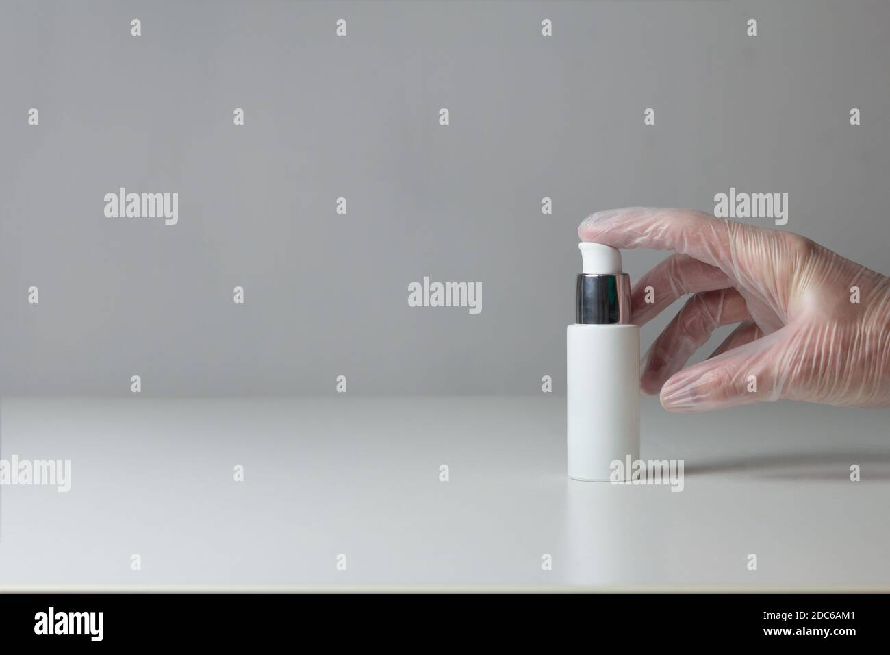 Un dito preme un vaso di gel disinfettante su uno sfondo grigio e un tavolo bianco. Foto Stock