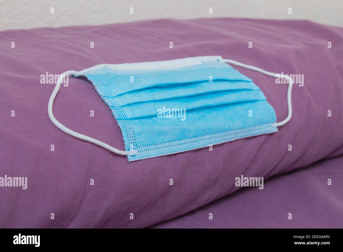 Un primo piano di una maschera chirurgica blu si trova su un cuscino viola. Foto Stock