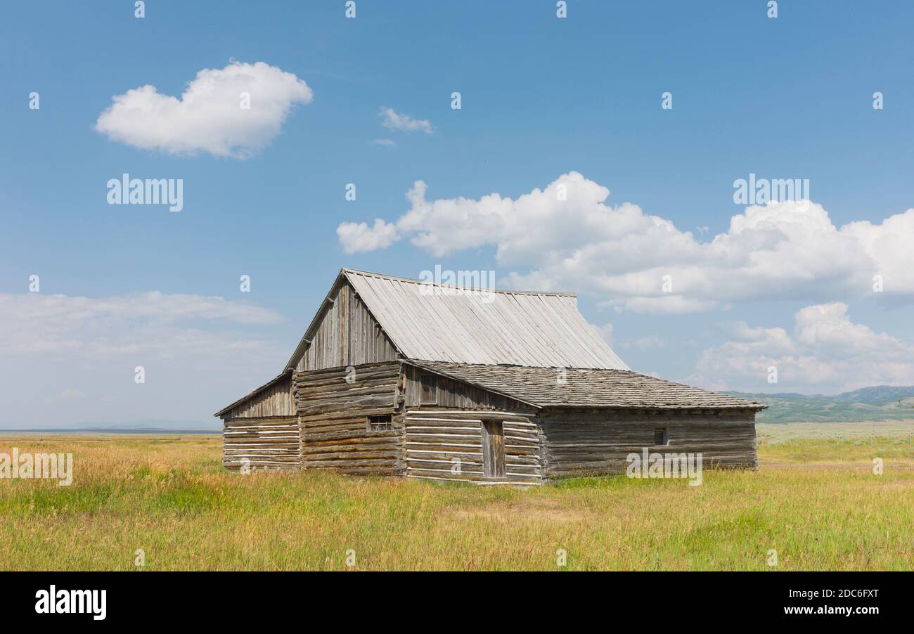 Casale dei coloni abbandonati nel mezzo della vasta prateria sotto il cielo azzurro e le nuvole in estate vicino a Jackson, Wyoming, USA. Foto Stock