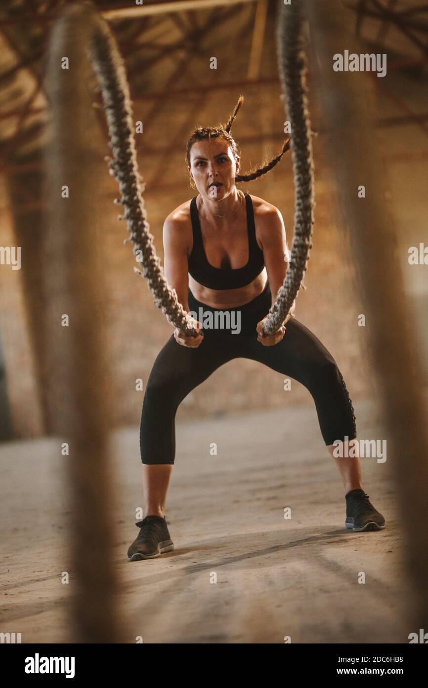 donna in forma fisica che si allena con la corda da battaglia. Donna dura che lavora all'ombra abbandonata della fabbrica. Foto Stock