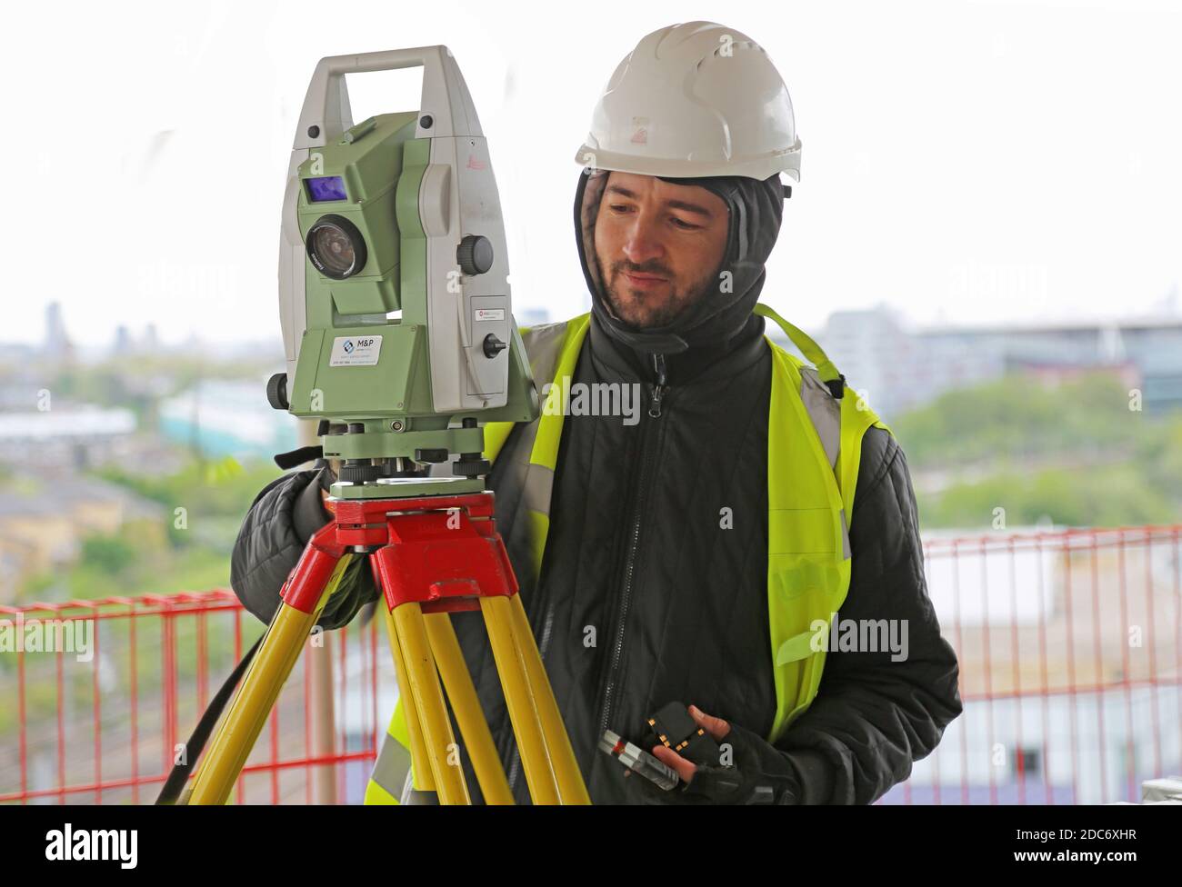 Un topografo di costruzione maschile regola una teodolite elettronica su un Grande sviluppo londinese Foto Stock