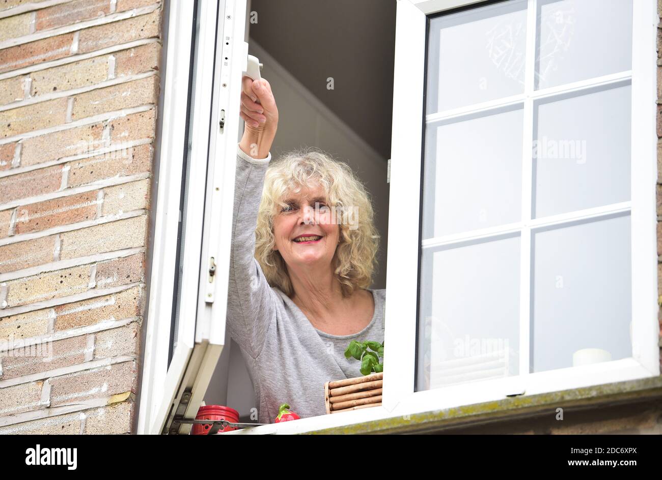 Donna a casa che apre la finestra della cucina per lasciare in fresco Air come consigliato per aiutare a combattere il virus COVID-19 del coronavirus Foto Stock