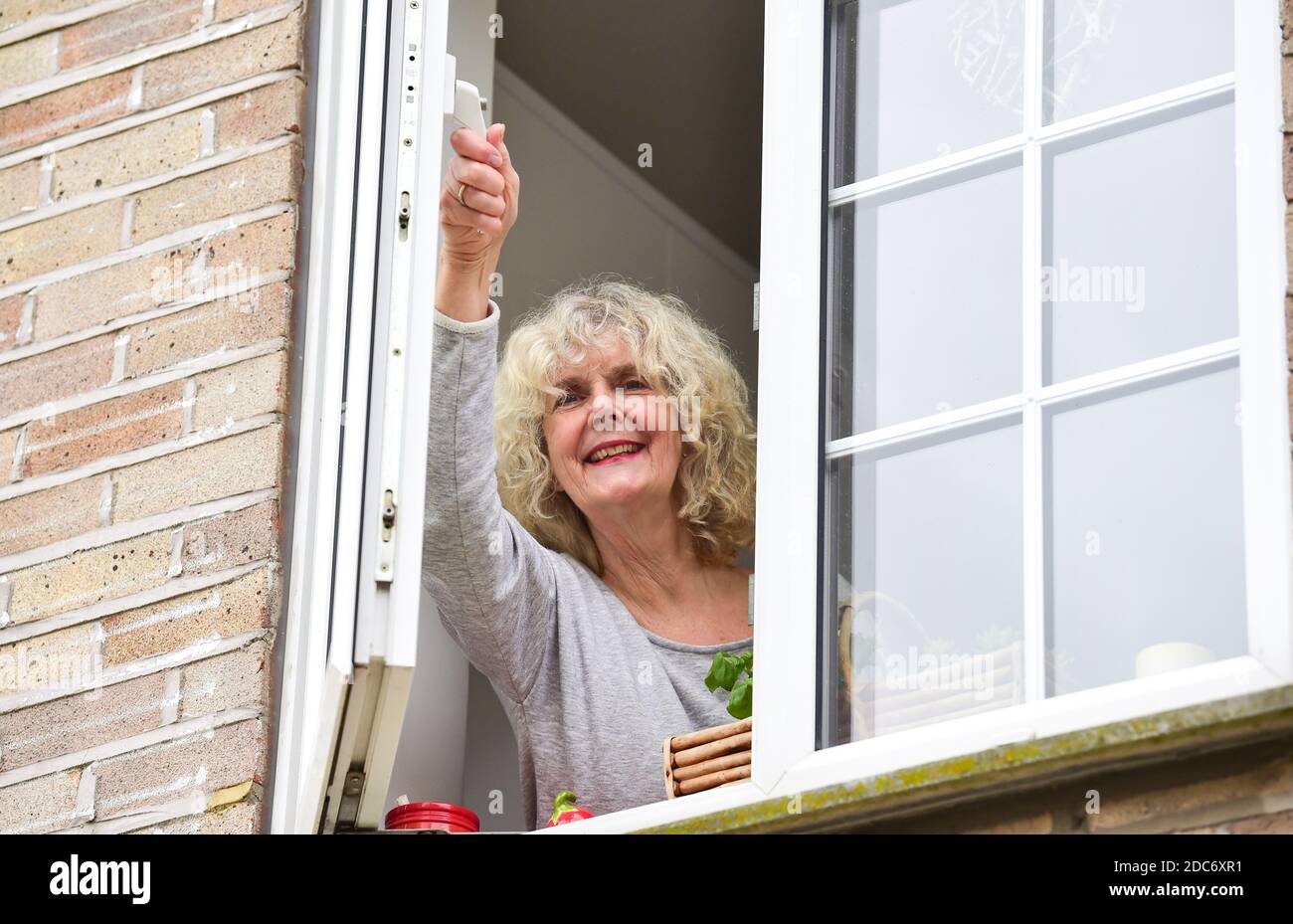 Donna a casa che apre la finestra della cucina per lasciare in fresco Air come consigliato per aiutare a combattere il virus COVID-19 del coronavirus Foto Stock