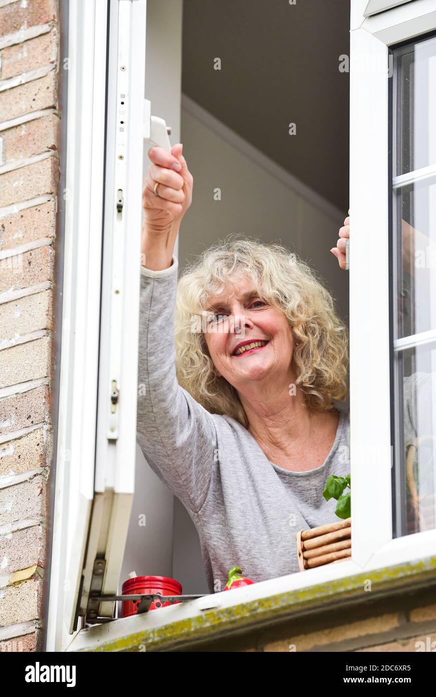Donna a casa che apre la finestra della cucina per lasciare in fresco Air come consigliato per aiutare a combattere il virus COVID-19 del coronavirus Foto Stock