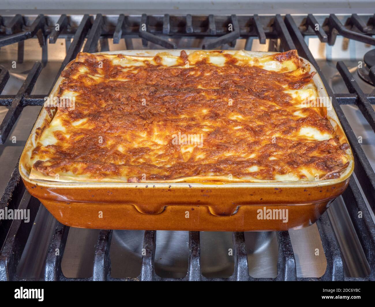 Primo piano POV di pasta fatta in casa, cucinata di fresco, bollente lasagne, in una piastra di cottura in ceramica, su un piano cottura. Foto Stock