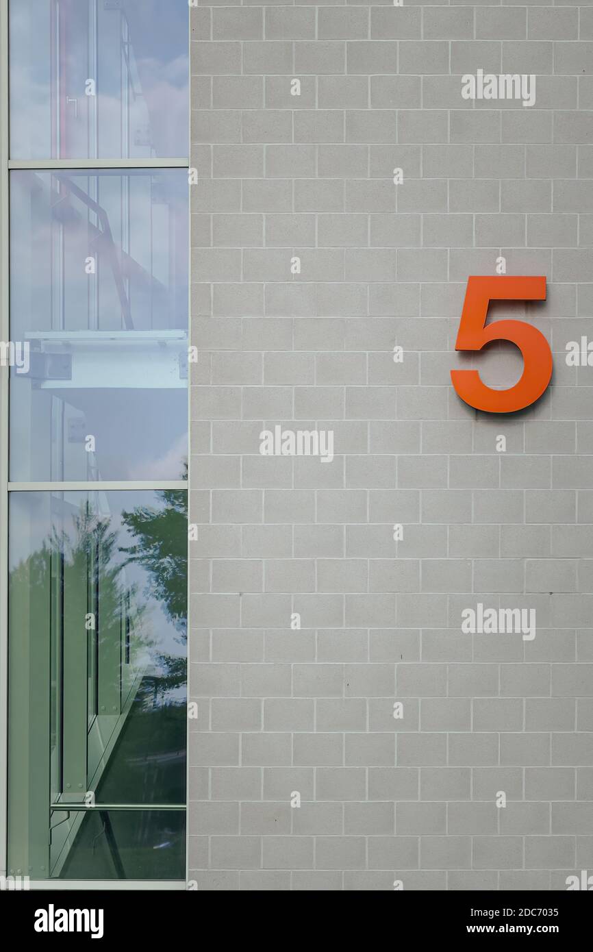 Casa arancione numero 5 sulla facciata esterna di un'architettura moderna con vetri ad angolo. Foto Stock