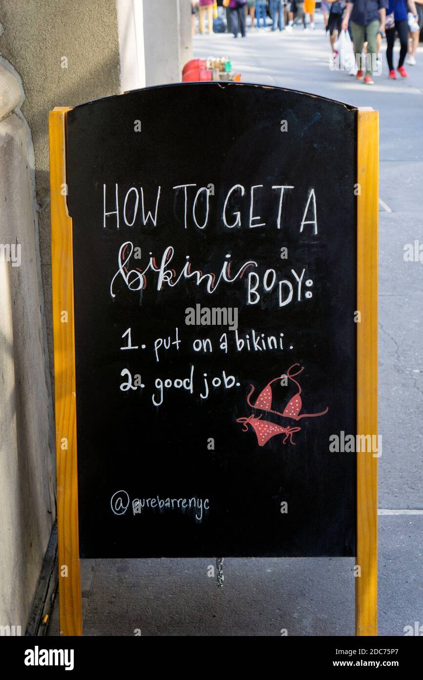 Un cartello all'esterno di una palestra DI PURO SBARRE che dice che il modo per ottenere un corpo bikini è metterne uno solo. Sulla Fifth Avenue a Manhattan, New York. Foto Stock