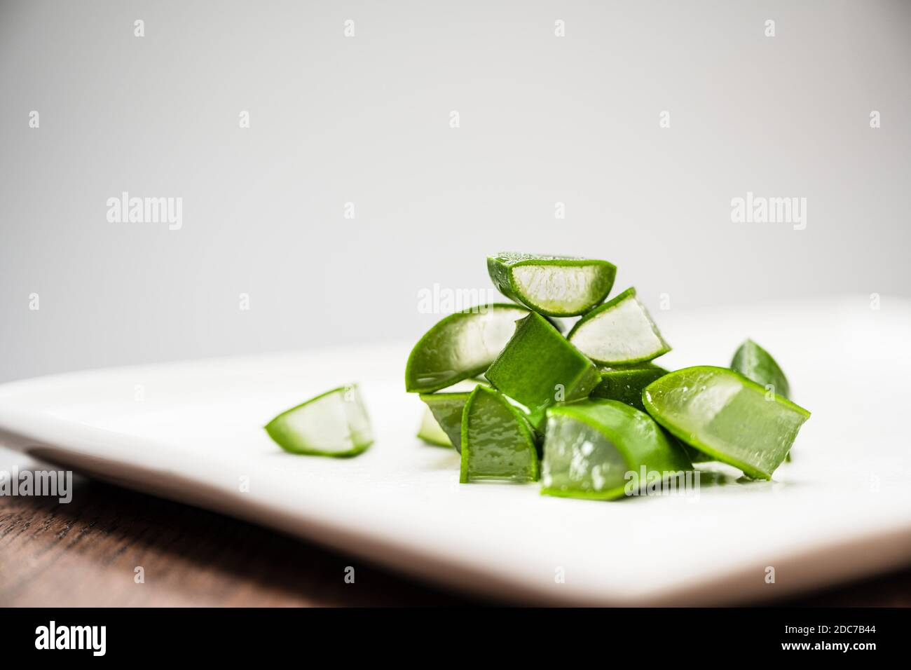 L'umidità e l'acqua sgocciolano dall'aloe fresco verde tagliato I pezzi di vera giacciono su un piatto bianco Foto Stock