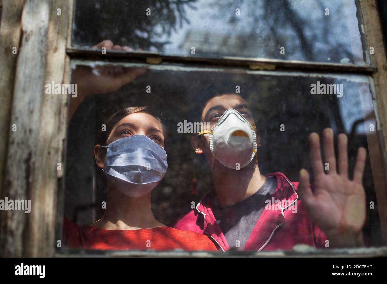 Famiglia in quarantena, giovane coppia caucasica indossare maschere mediche di protezione guardando attraverso La finestra, Coronavirus Covid-19 malattia del virus pandemia Foto Stock