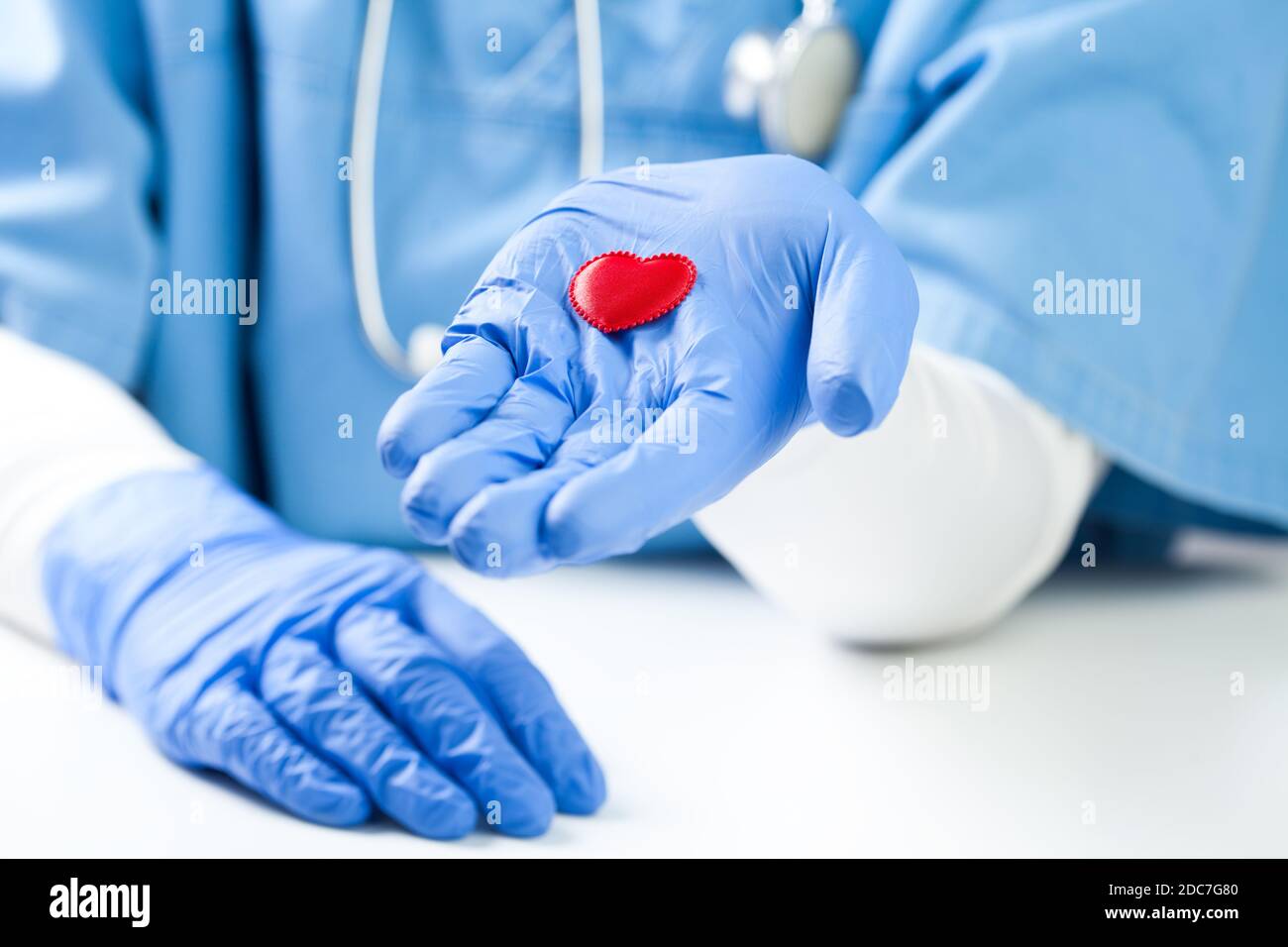 Medico femminile che tiene piccolo cuore rosso sul palmo della mano, indossando uniforme blu NHS, dettaglio primo piano, frequenti controlli sanitari e prevenzione delle malattie Foto Stock