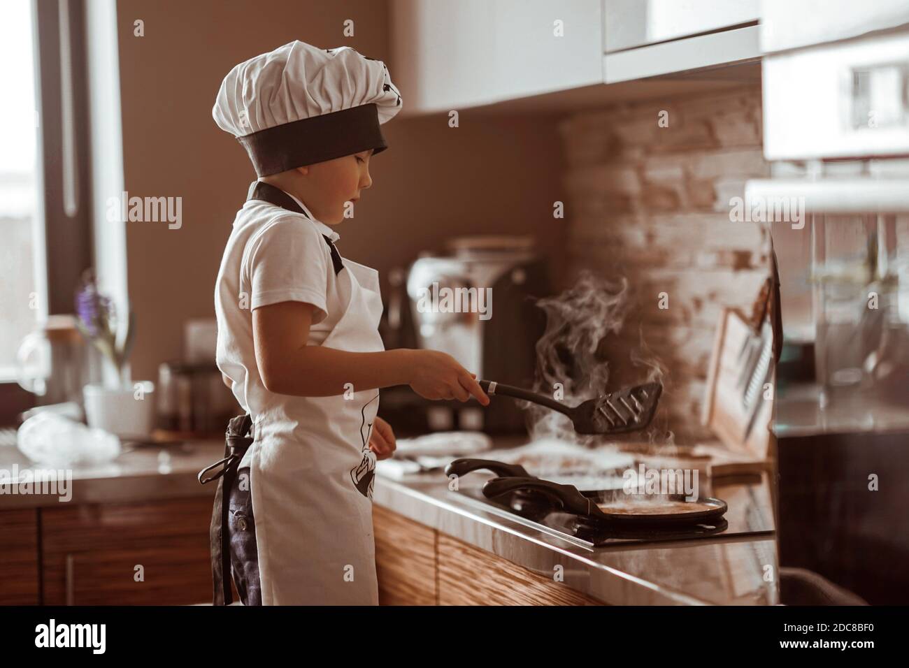 Un ragazzino cuoce le frittelle in cucina Foto Stock