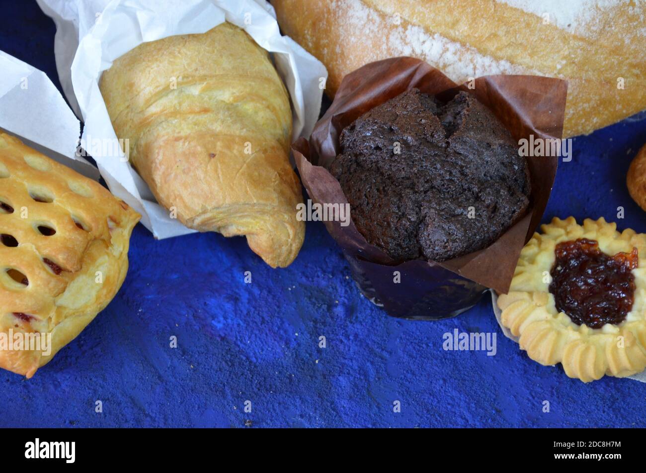 Diversi tipi di panini su sfondo blu scuro dall'alto. Poster da cucina o da forno. Muffin, croissant, biscotti con patatine al cioccolato Foto Stock