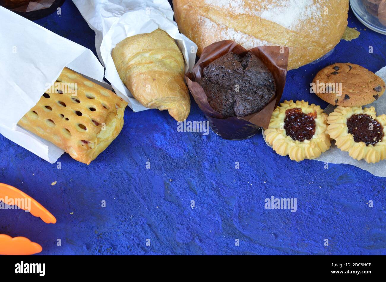 Diversi tipi di panini su sfondo blu scuro dall'alto. Poster da cucina o da forno. Muffin, croissant, biscotti con patatine al cioccolato Foto Stock