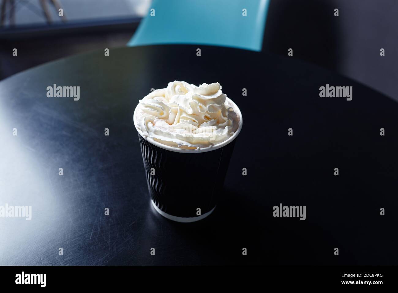 Tazza di carta monouso con gustosa bevanda a base di caffè con latte e panna montata su un tavolo di legno nel caffè. Messa a fuoco selettiva, sfondo sfocato Foto Stock