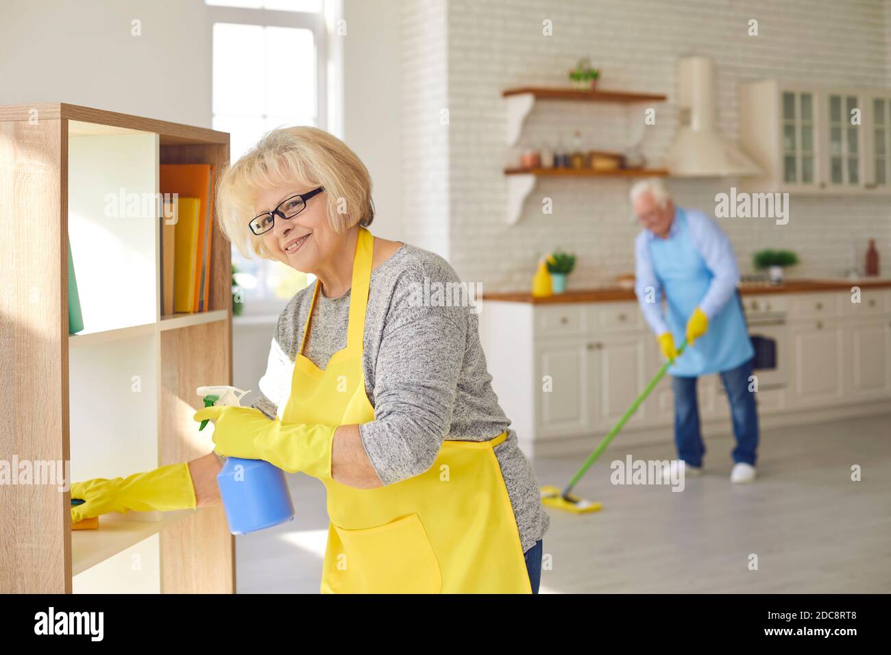 Felice uomo e donna di coppia senior in grembiuli e guanti pulizia a casa Foto Stock