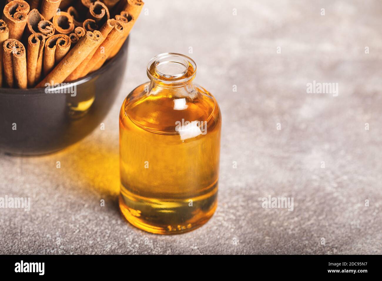 Olio essenziale di cannella in una piccola bottiglia, cannella macinata e bastoncini di cannella su fondo di pietra. Foto Stock