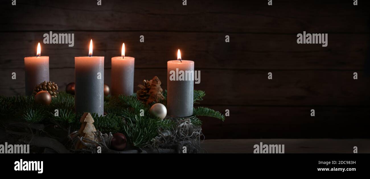 Quattro candele brucianti su una corona d'Avvento da rami d'abete con decorazione di Natale contro una parete di legno scuro rustico, formato panoramico con copia spa Foto Stock