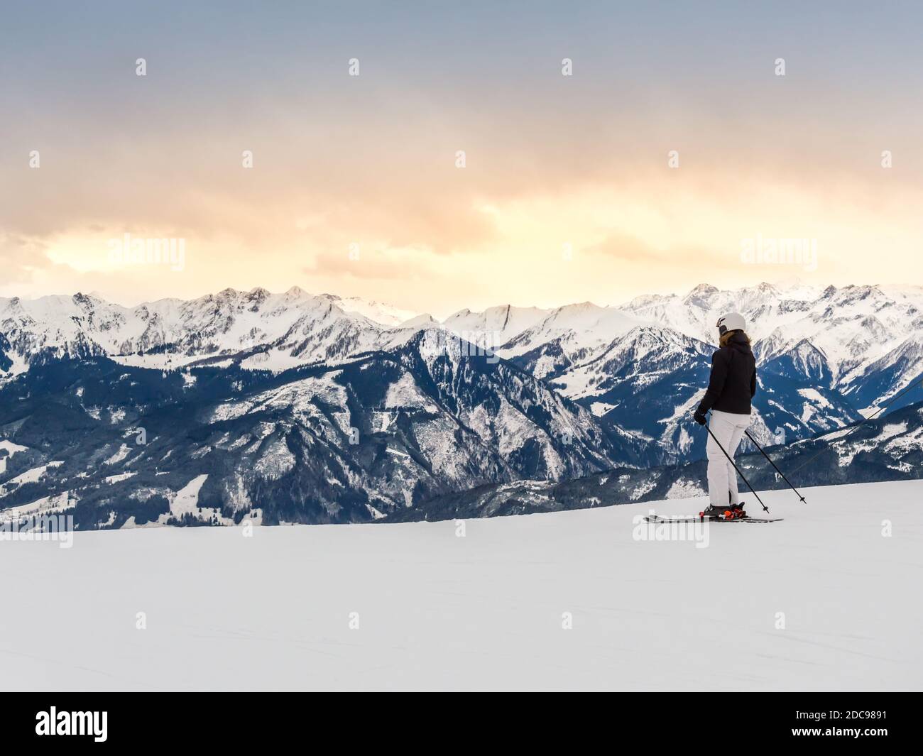 Sciatore femminile in pendenza contro le montagne e il tramonto nella stazione sciistica invernale Zell am See nelle Alpi, Austria. La catena montuosa di Kitzsteinhorn Foto Stock