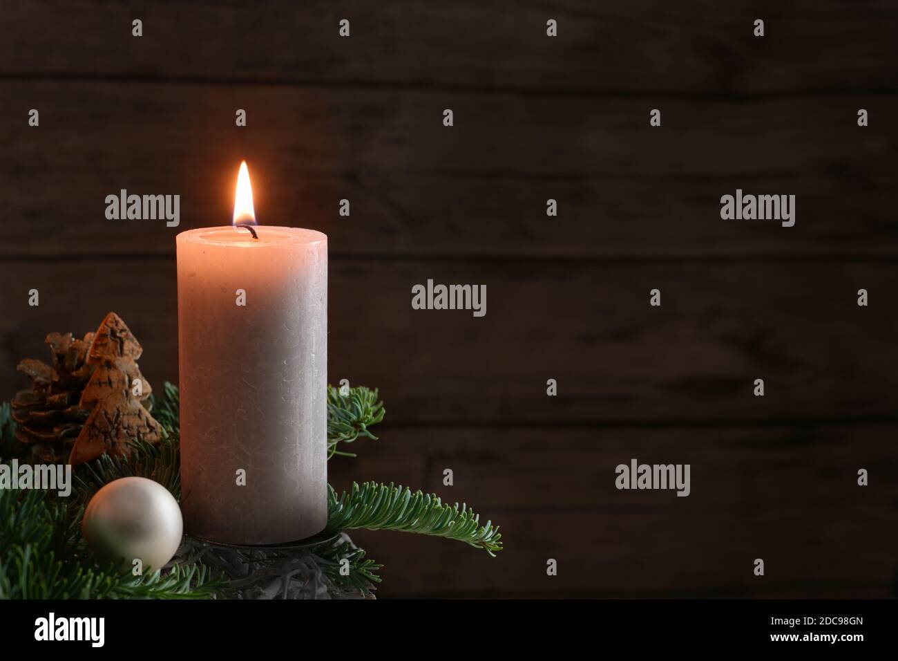 Candela bruciante su rami di abete con palla di Natale e decorazione contro una parete rustica di legno, luce dell'avvento nella stagione scura, spazio di copia, selezionato Foto Stock