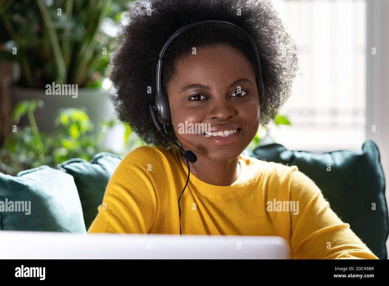 Sorridente consulente afroamericano donna indossare cuffie guardando la fotocamera mentre il lavoro remoto sul computer durante il blocco. E-business, assistenza clienti s Foto Stock