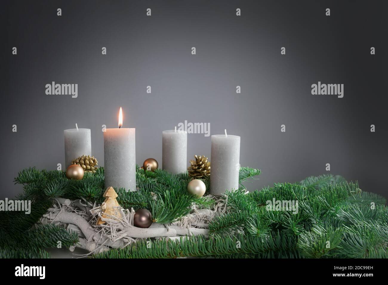 Una delle quattro candele sta bruciando per il primo Avvento su rami di abete con decorazione di Natale contro uno sfondo grigio, spazio di copia, fuoco selezionato, n Foto Stock