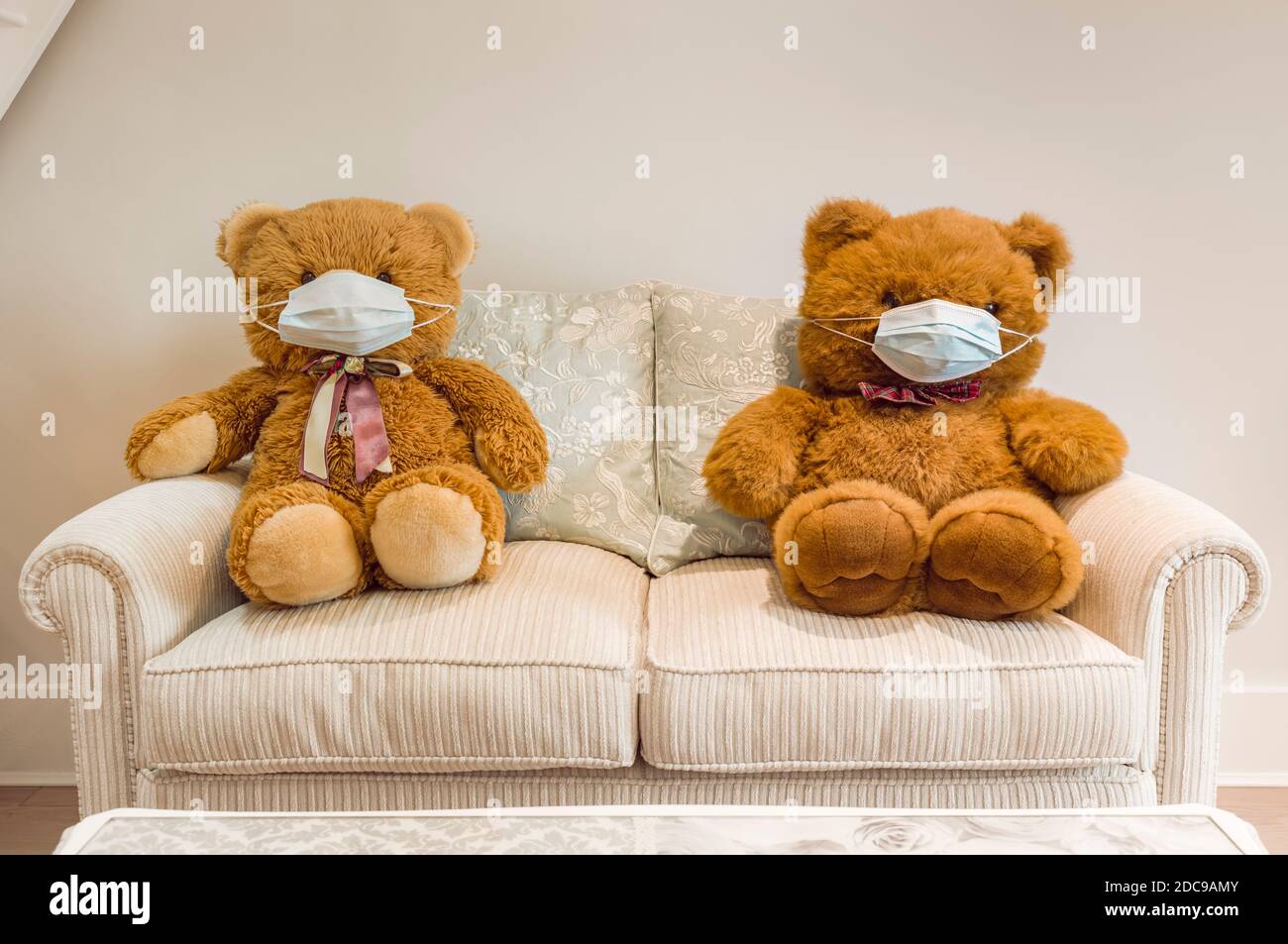 Gli orsi Teddy indossano maschere sul viso seduti su un divano, a distanza sociale. Ideale per i bambini, COVID-19 concetto di distanza sociale coronavirus. Foto Stock