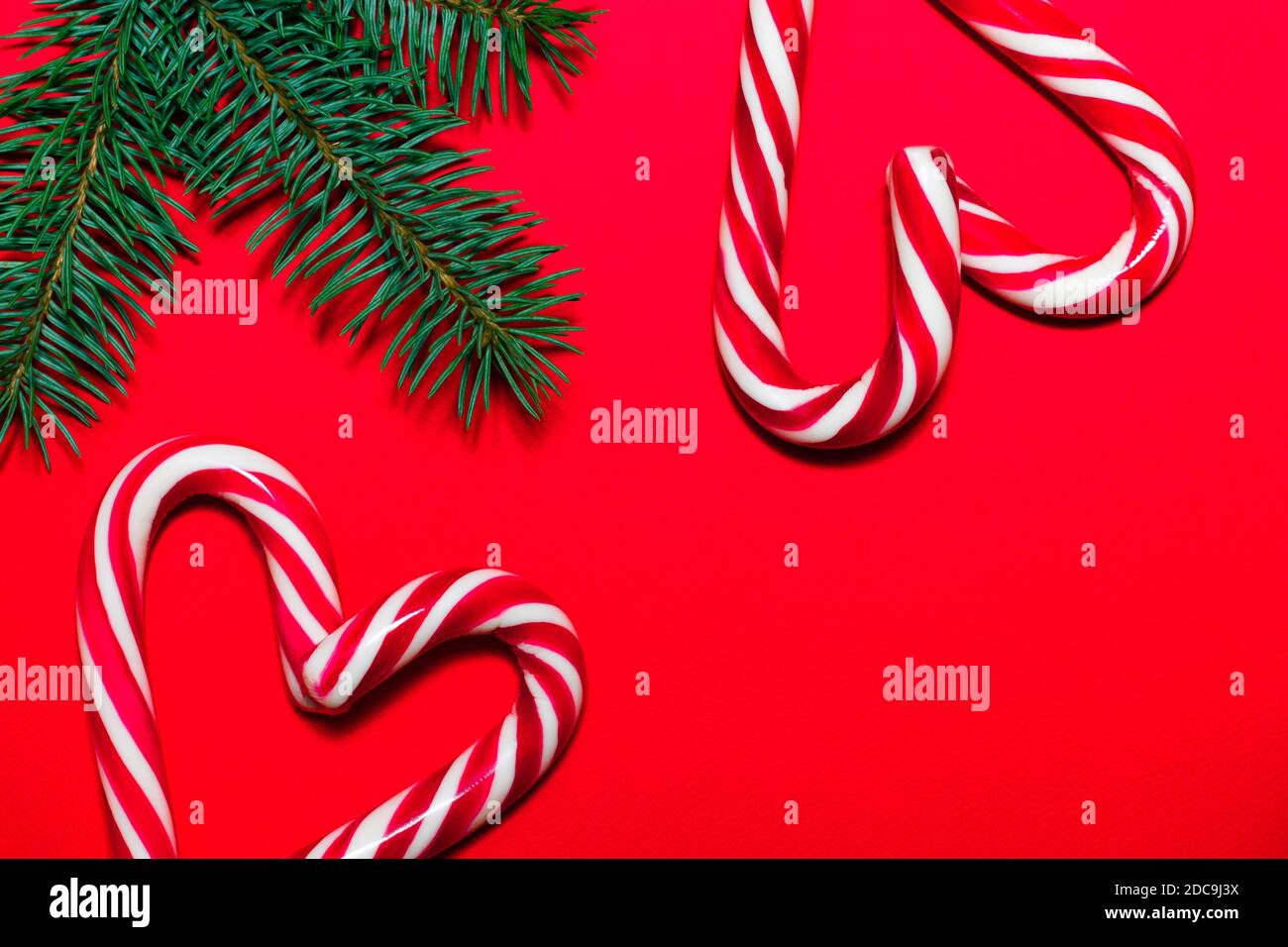 Cuori di Lollipop su superficie rossa con rami di albero di Natale. Biglietto d'auguri per Natale e Capodanno Foto Stock