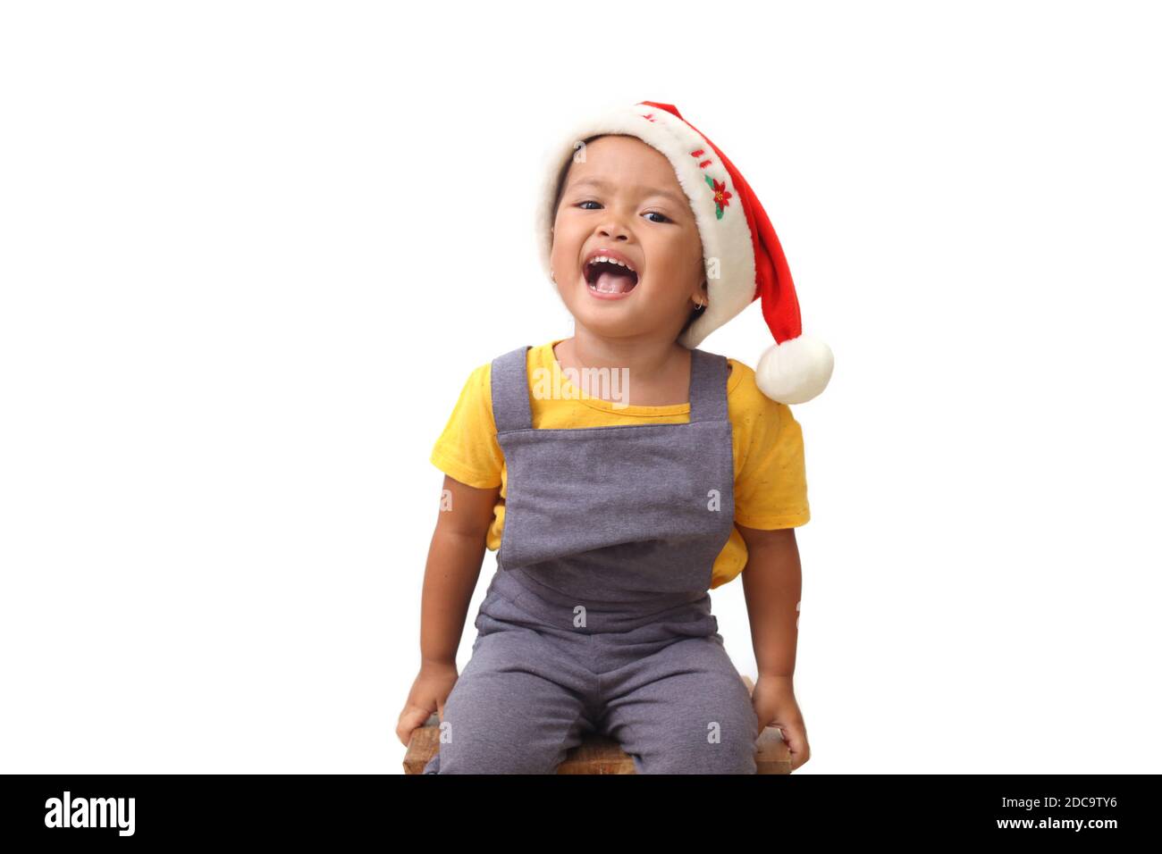 Adorabile ragazza asiatica seduta mentre indossa il cappello di babbo natale. Concetto di Natale per bambini. Isolato su sfondo bianco Foto Stock