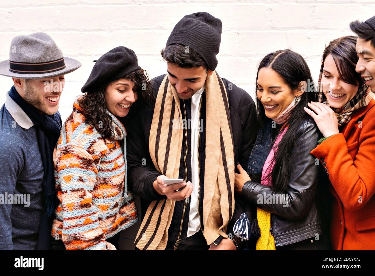 Gruppi di giovani adulti si riuniscono su uno smartphone - Abbigliamento invernale - stagionale - Divertimento Foto Stock