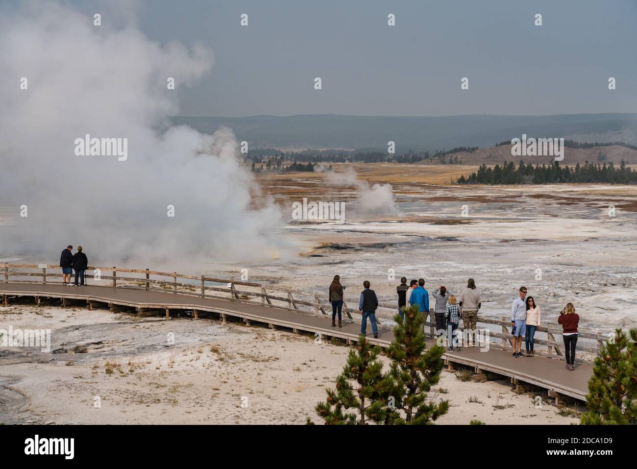 I turisti guardano il Geyser Clepsydra che emette vapore nel bacino inferiore del Geyser nel Parco Nazionale di Yellowstone, Wyoming, Stati Uniti. Foto Stock