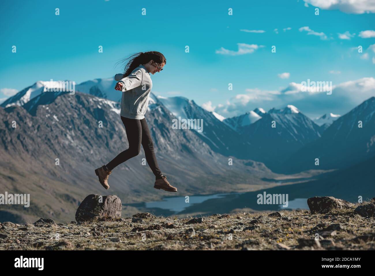 Una ragazza snella e sportiva si diverte e salta sopra la pietra in alta montagna. Concetto di turismo attivo Foto Stock
