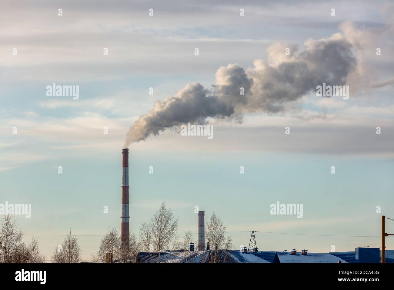 Colpo di tetti e tubi di impianto di riscaldamento che forniscono il sistema di riscaldamento centrale della città. Fumo che esce dai tubi. Cielo blu nuvoloso come sfondo Foto Stock