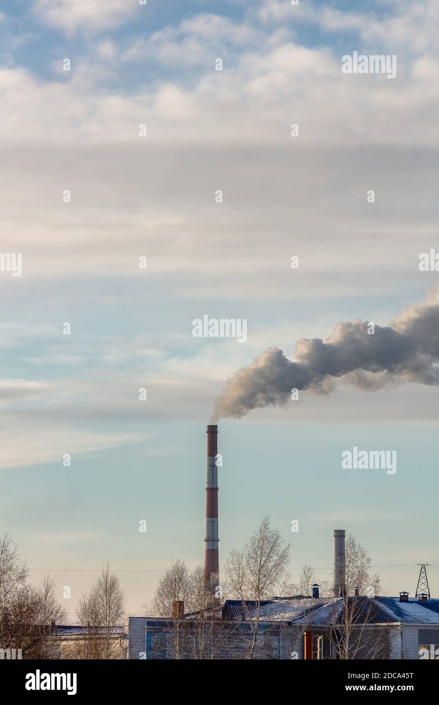 Colpo di tetti e tubi di impianto di riscaldamento che forniscono il sistema di riscaldamento centrale della città. Fumo che esce dai tubi. Cielo blu nuvoloso come sfondo Foto Stock