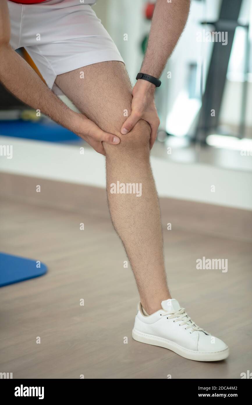 Primo piano delle mani maschili massaggiando il ginocchio doloroso Foto Stock