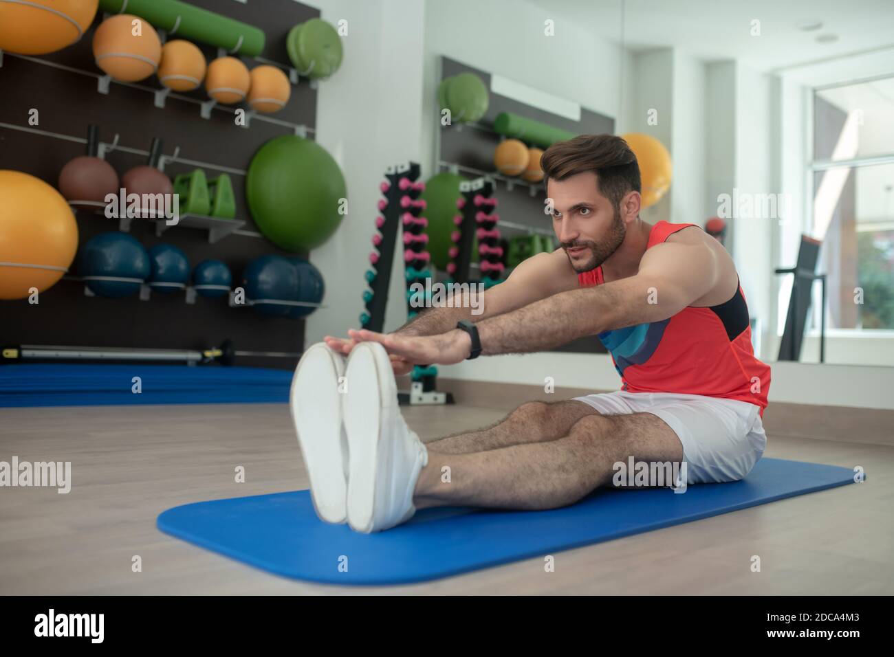 Maschio bearded che si piega in avanti, toccando le dita dei piedi, allungando le corde Foto Stock