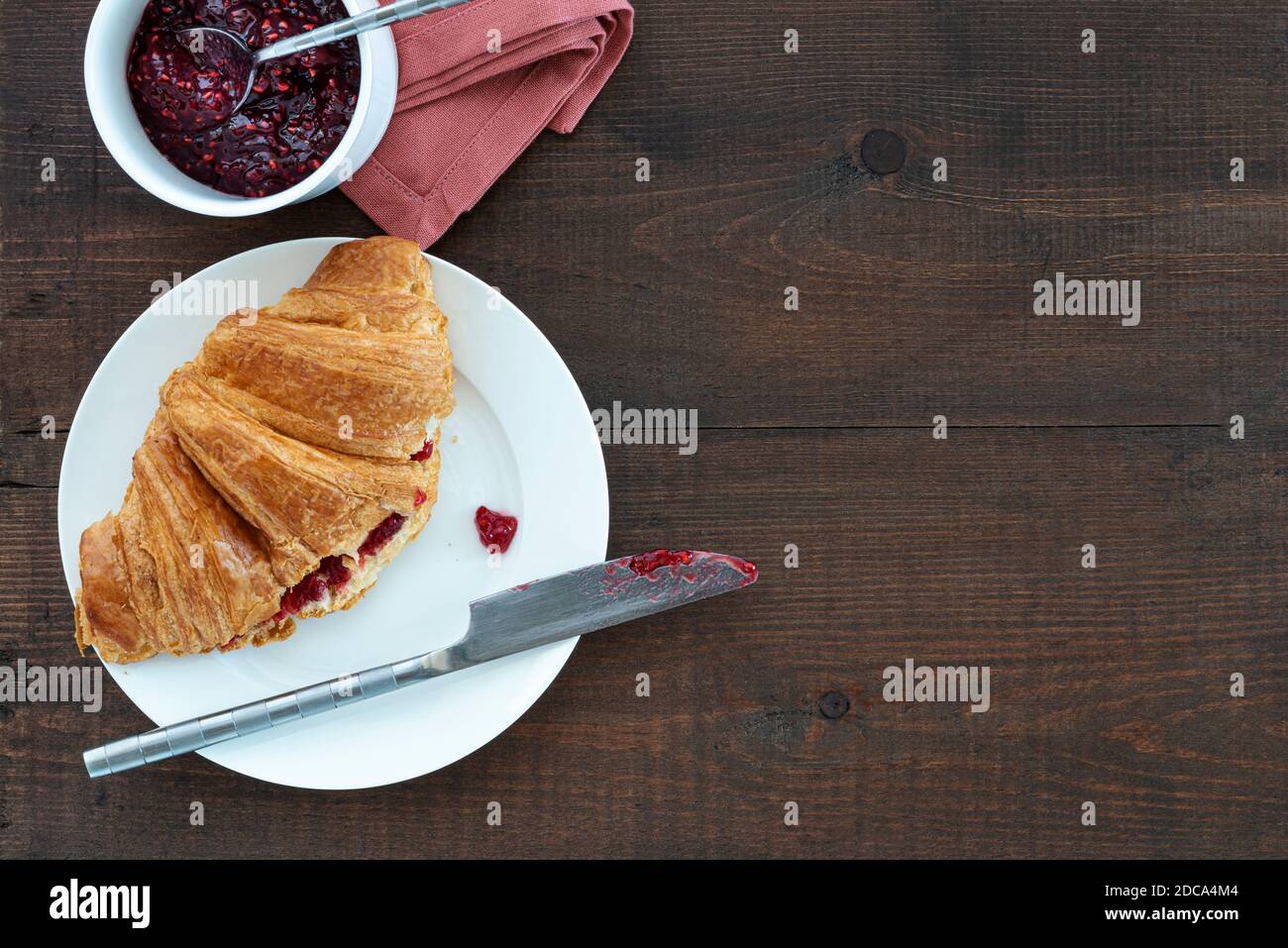 Croissant ripieno di marmellata su un piatto, con una pentola di conserve. Posto su un tavolo di legno. Foto Stock