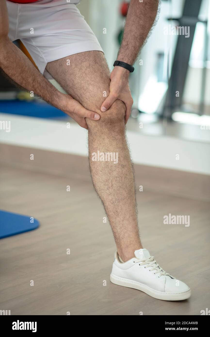 Primo piano delle mani maschili massaggiando il ginocchio doloroso Foto Stock