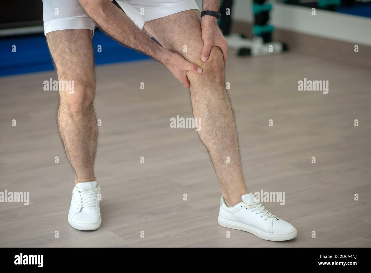 Primo piano di mani maschili che massaggiano il ginocchio doloroso in palestra Foto Stock
