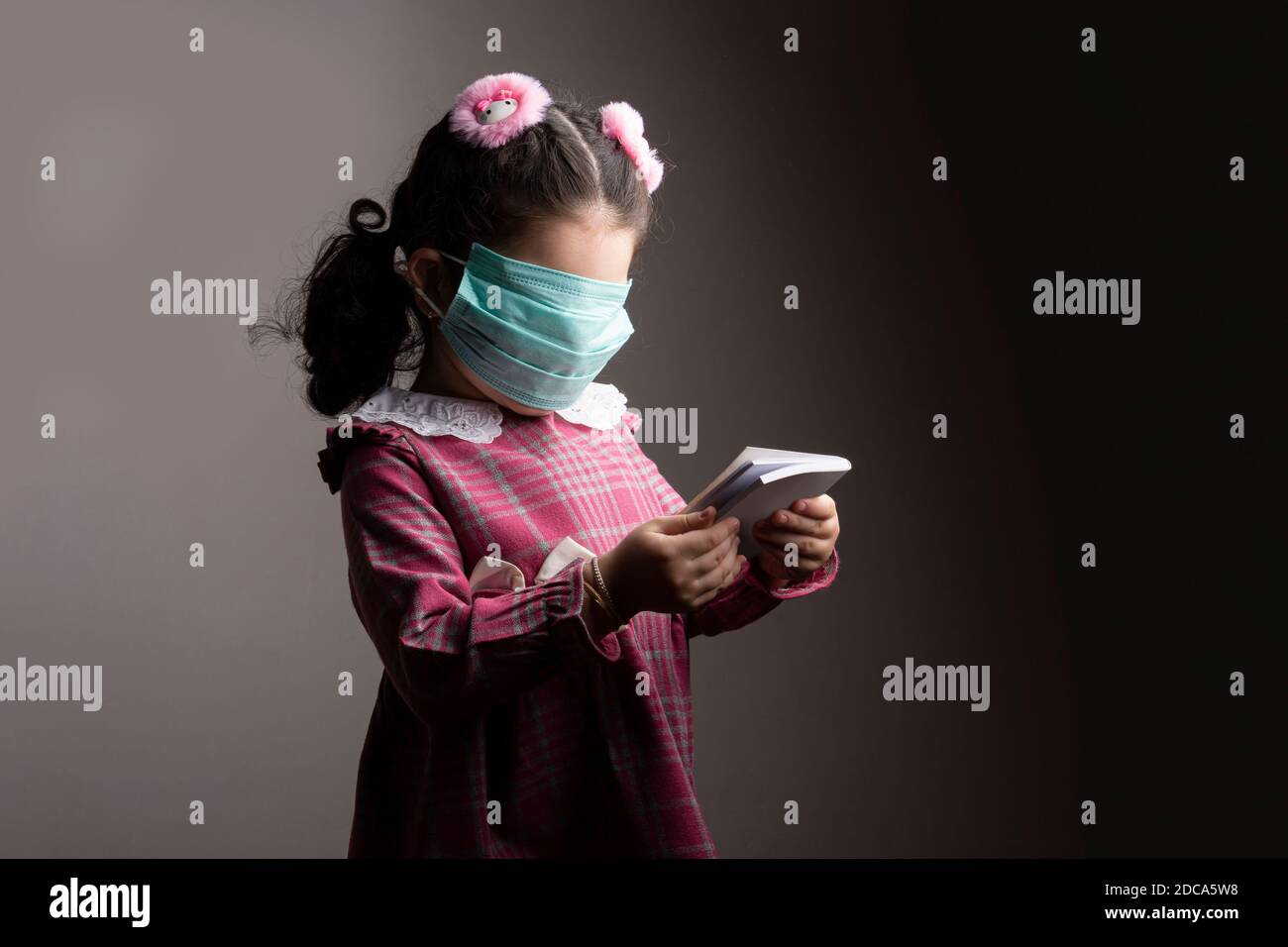 Volto coperto di una bambina con maschera di protezione ospedale quando si studia un libro, anonimato e cecità concetto Foto Stock