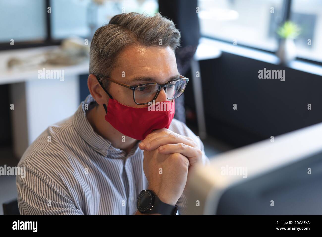 Uomo caucasico che indossa la maschera facciale guardando lo schermo del computer in ufficio Foto Stock