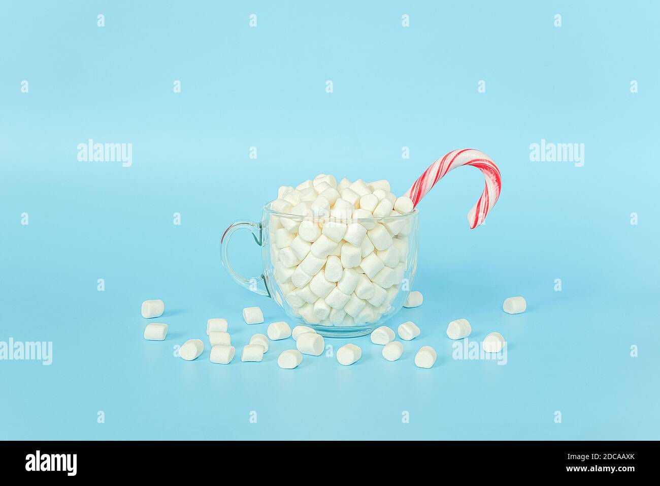 Grande tazza trasparente di marshmallows con canna di lecca rossa su fondo blu. Buon Natale o buon anno concetto. Stile minimal, vista dall'alto, FLA Foto Stock