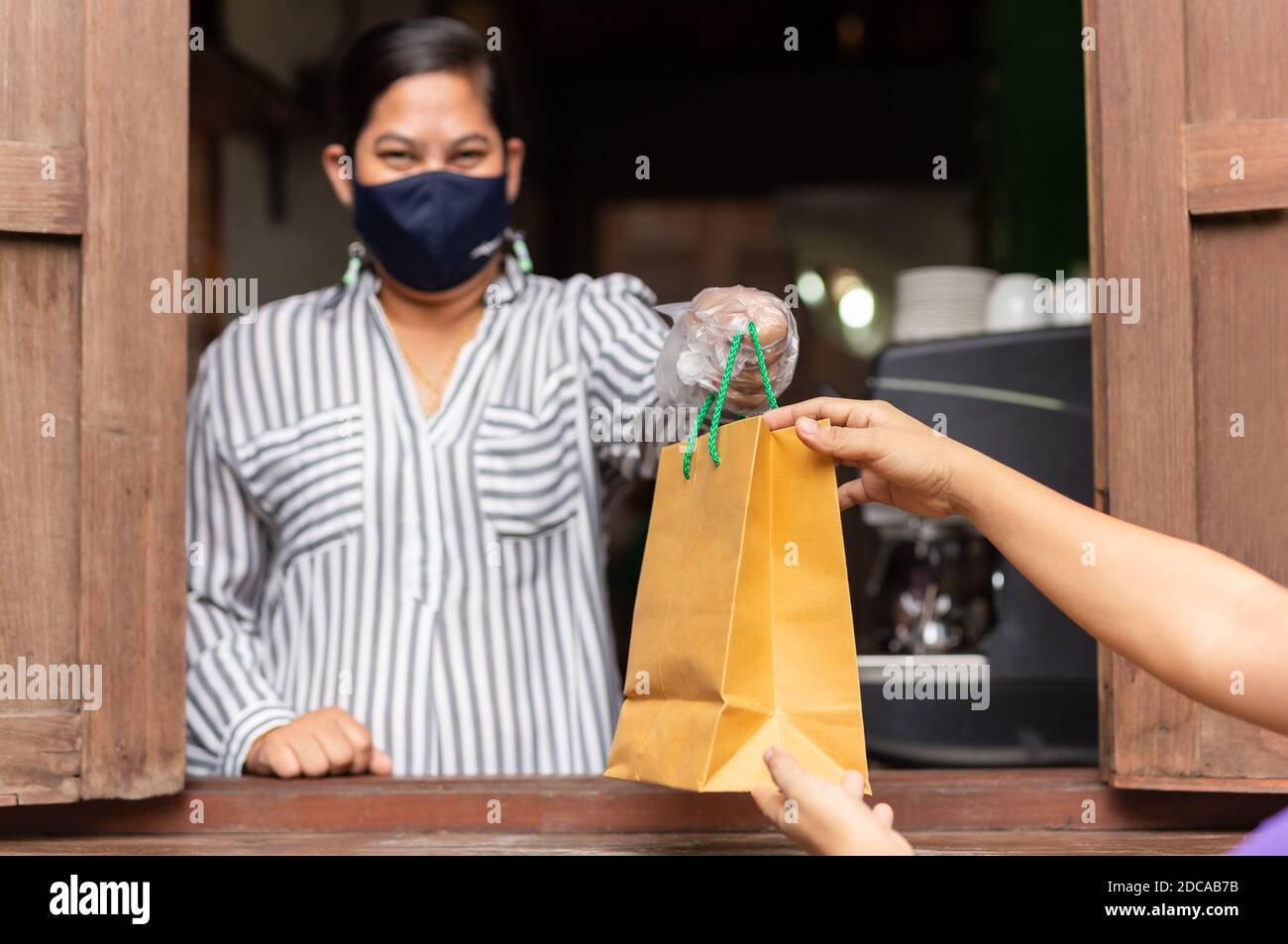 Cameriera concettuale a distanza sociale che dà una borsa da asporto al cliente al bar. Foto Stock