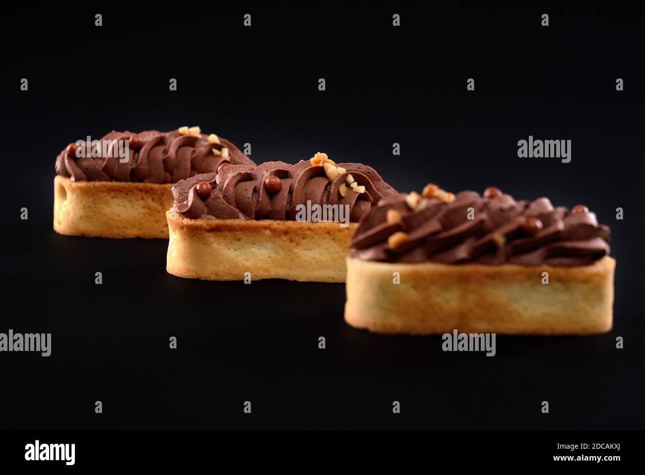 Biscotti frollini con panna di cioccolato marrone montata con mascarpone. Tre dolci freschi fatti in casa isolati su sfondo nero. Concetto di dolci, industria alimentare. Foto Stock