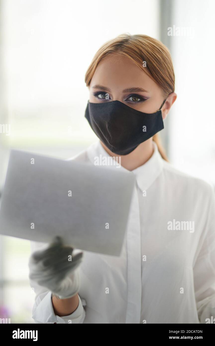 Giovane donna in maschera faccia tenere bianco tavola vuota accanto alla porta di vetro Foto Stock