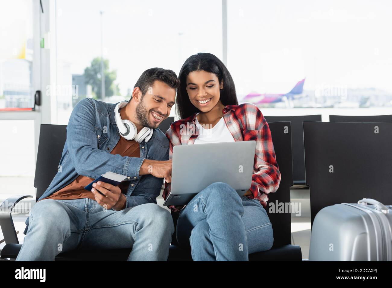 felice coppia interracial che guarda il laptop in aeroporto Foto Stock