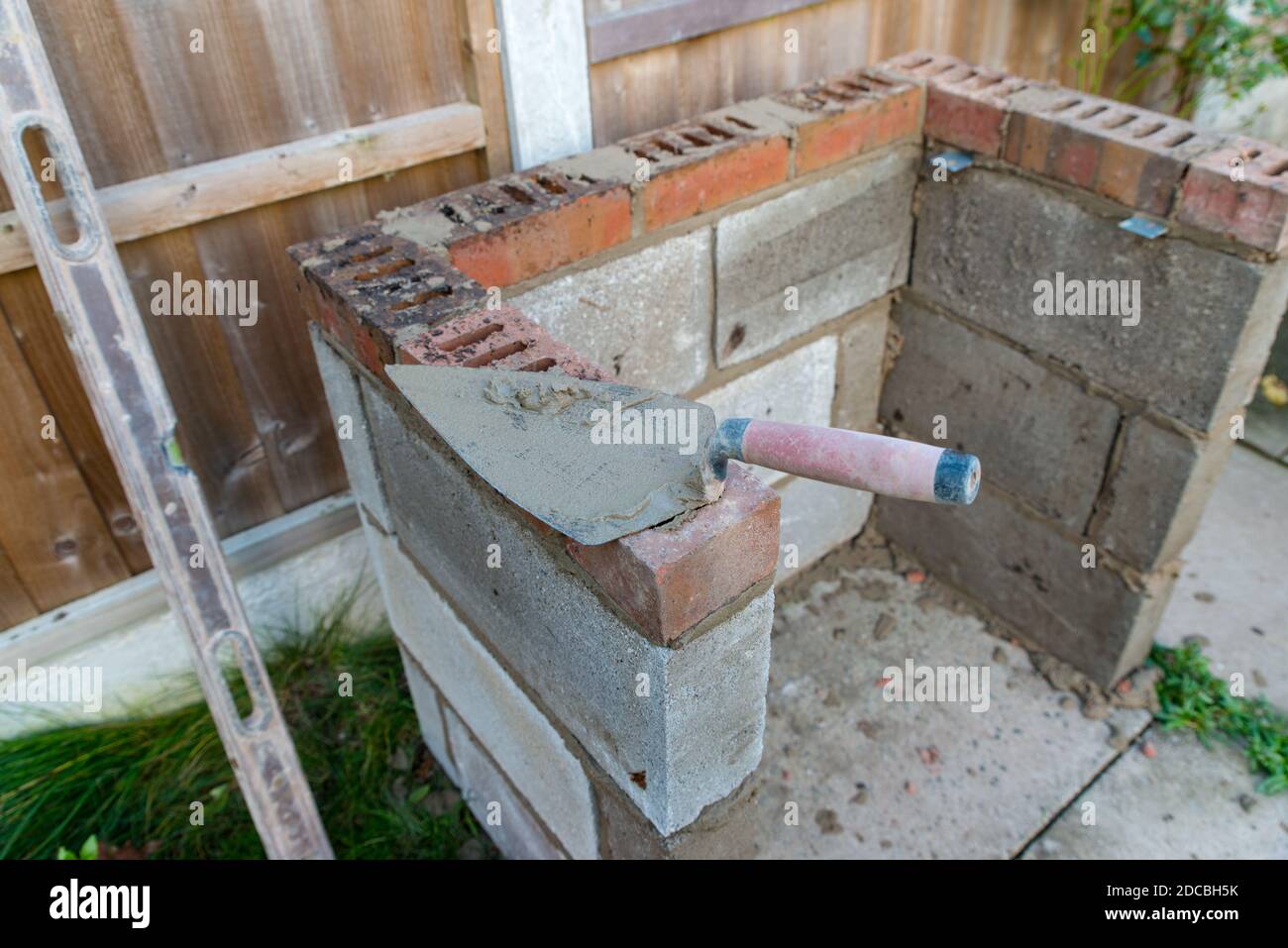 primo piano di cazzuola di muratore su mattoni, la costruzione di un barbecue fuori in autunno Foto Stock