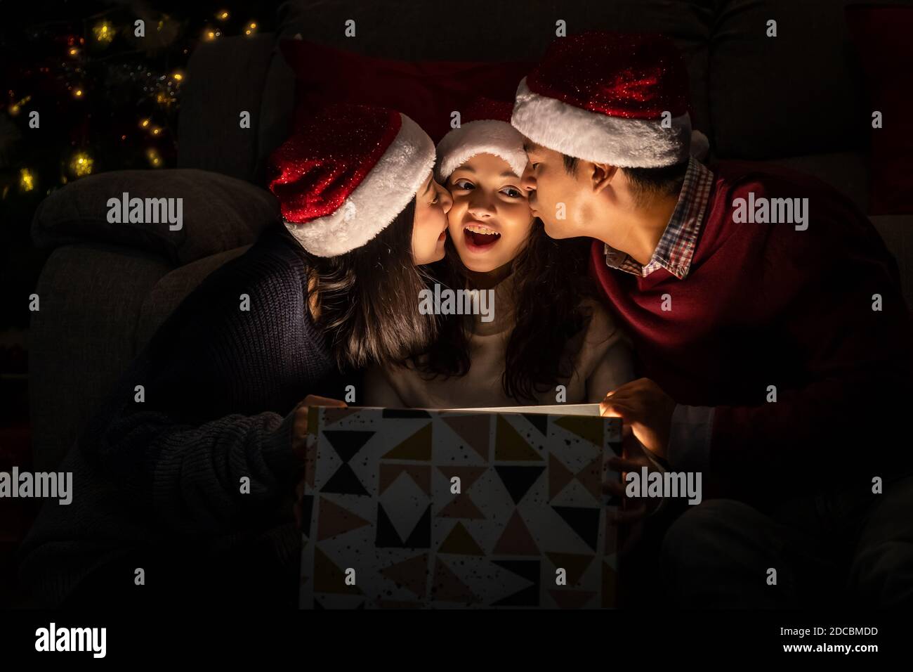 Felice ritratto di famiglia, padre madre e figlia, celebrare insieme Natale e Capodanno, apertura confezione regalo con magicamente sorpresa Foto Stock