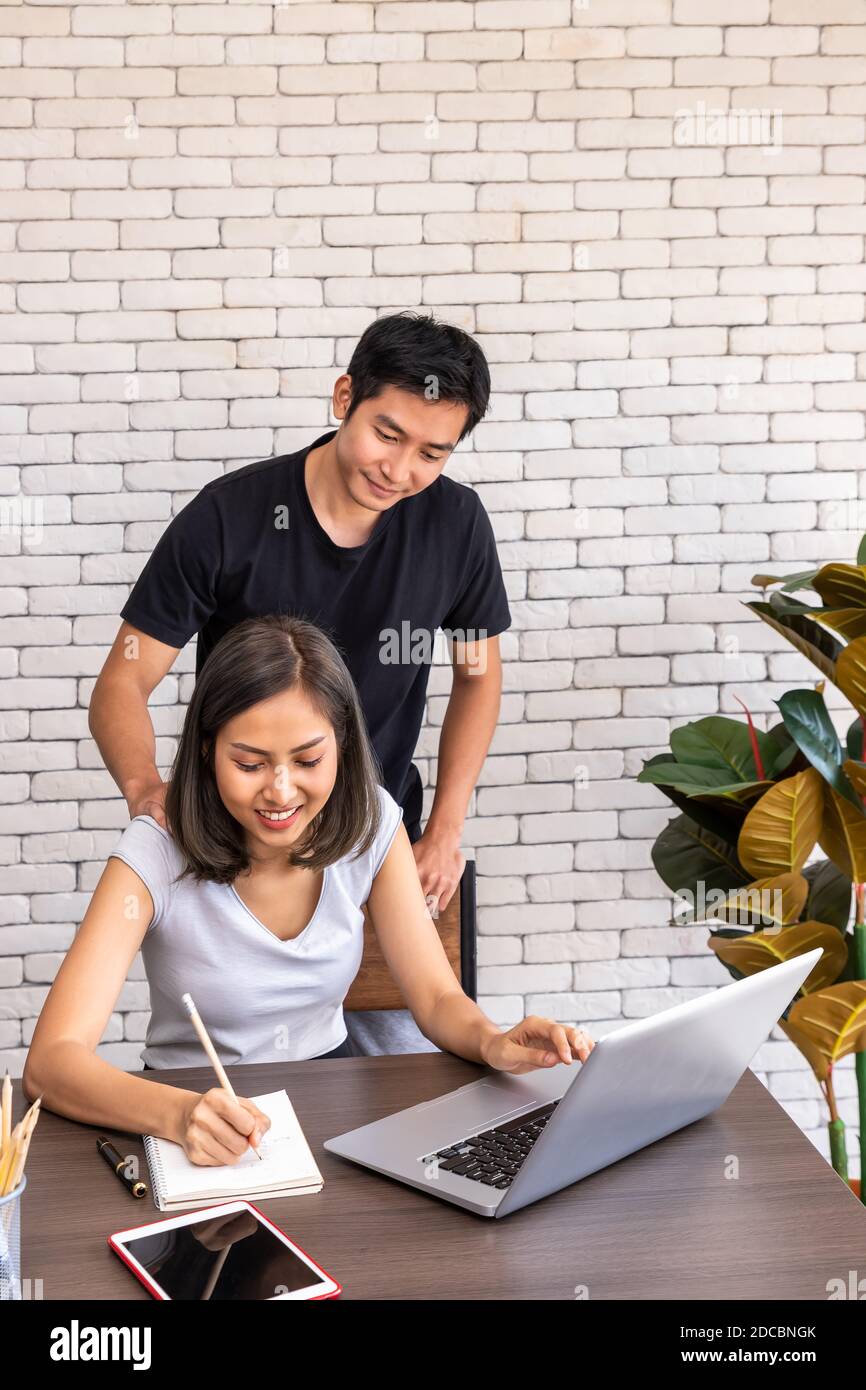Uomo asiatico marito motivare il sostegno moglie donna freelancer lavorare a casa, seduto al tavolo da pranzo scrivania in soggiorno Foto Stock